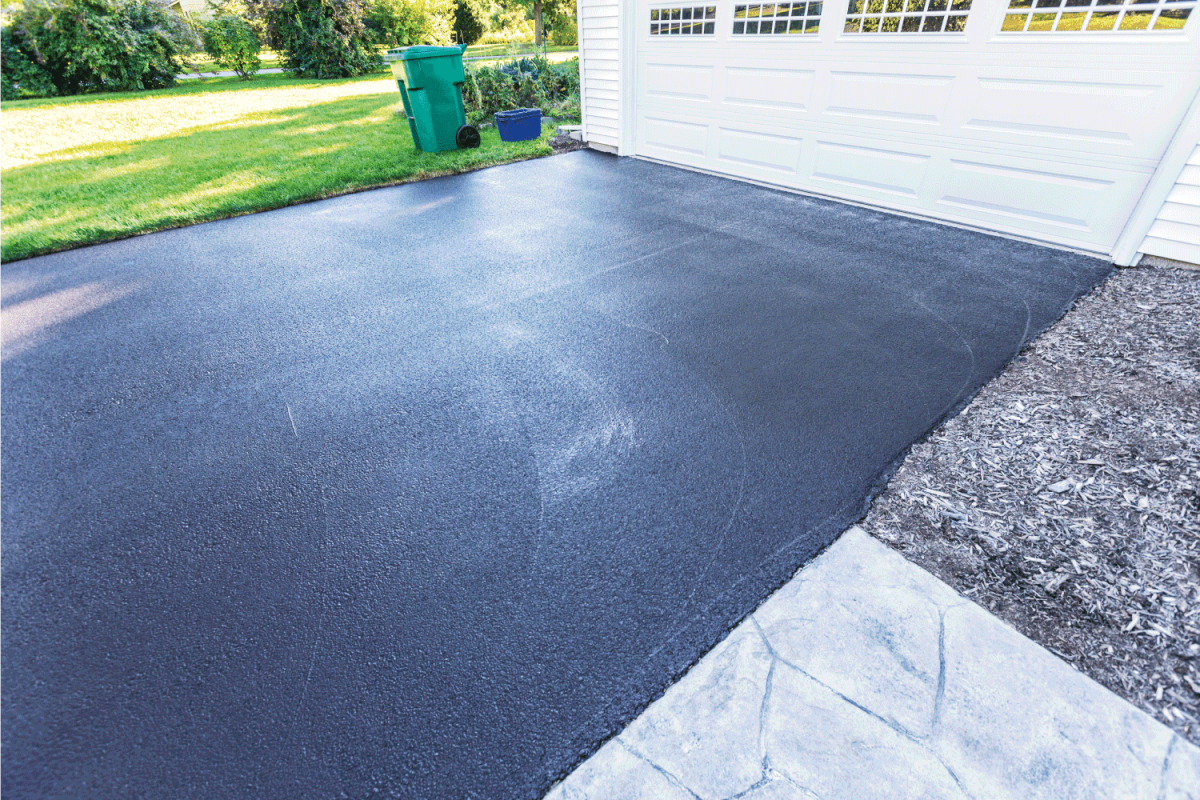 A fresh blacktop resealing job just finished on this asphalt driveway in a suburban residential district.