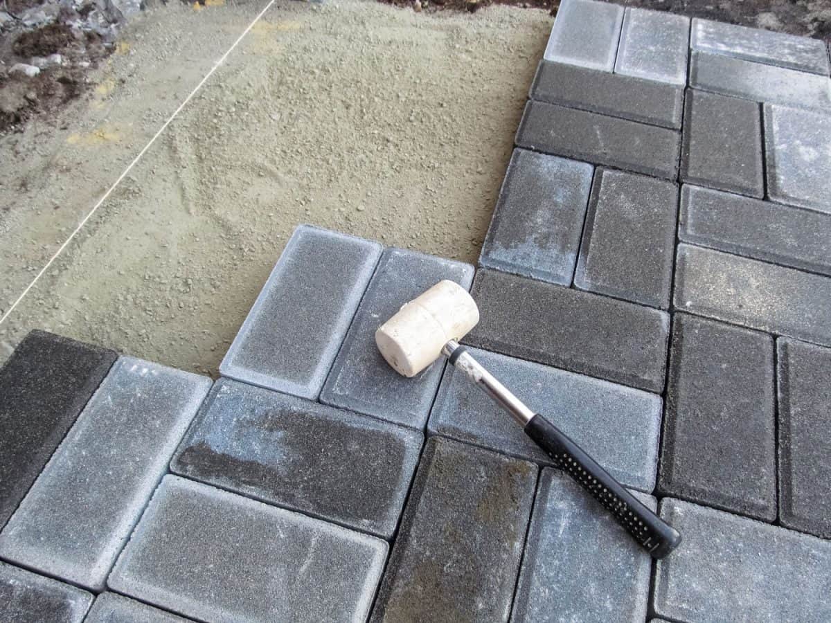 A white rubber mallet lies on the surface of a gray Brick paving slab 