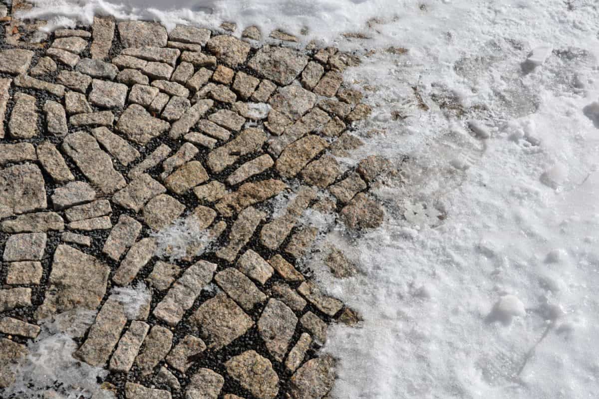 Brown granite paving of irregular stones. Frozen partially snow covered country road courtyard at the entrance to the building