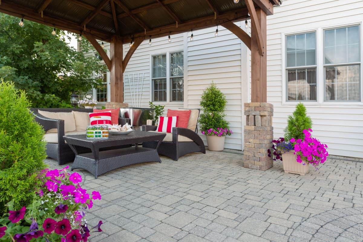 Brussel block design pavers on an exterior patio and summer living space with a covered gazebo, colorful petunias and comfortable seating