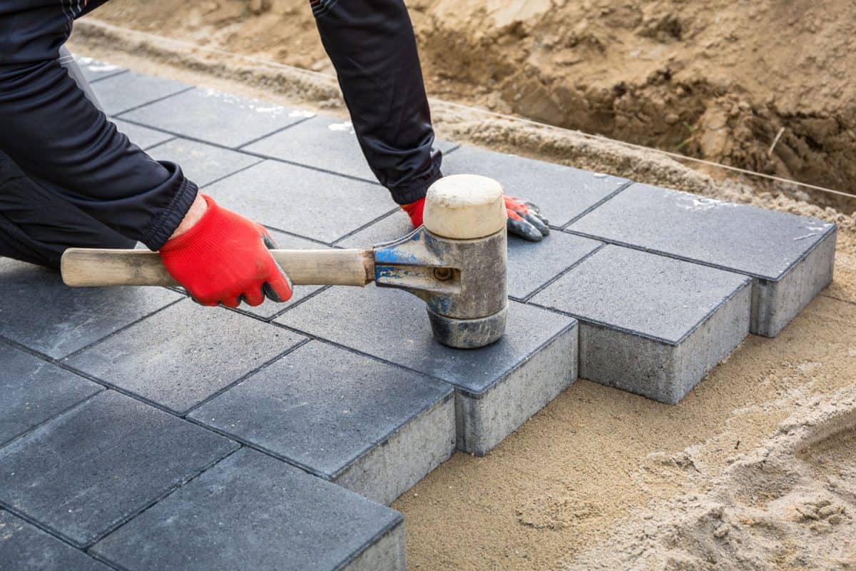 How Long to Wait to Seal Pavers, Hands of worker installing concrete paver blocks with rubber hammer