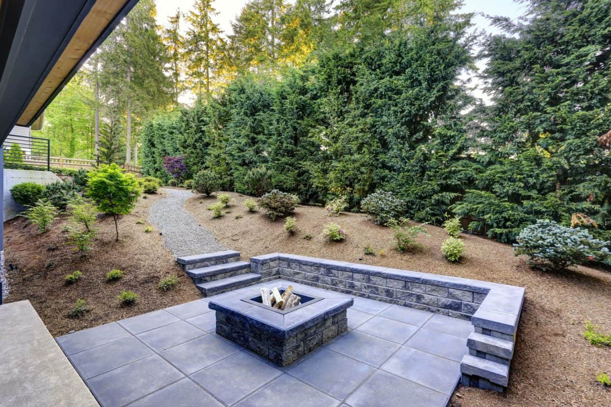 New modern home features a backyard with rectangular concrete fire pit framed by slate pavers and overlooking the lush garden, Should You Rinse Bleach Off Concrete?