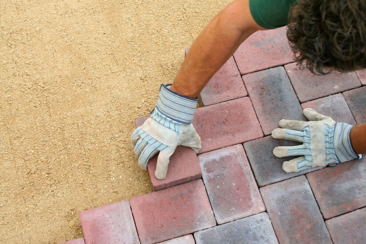 Pavement installer placing brick pavers for the patio, Can Polymeric Sand Be Reapplied? [And How Often]