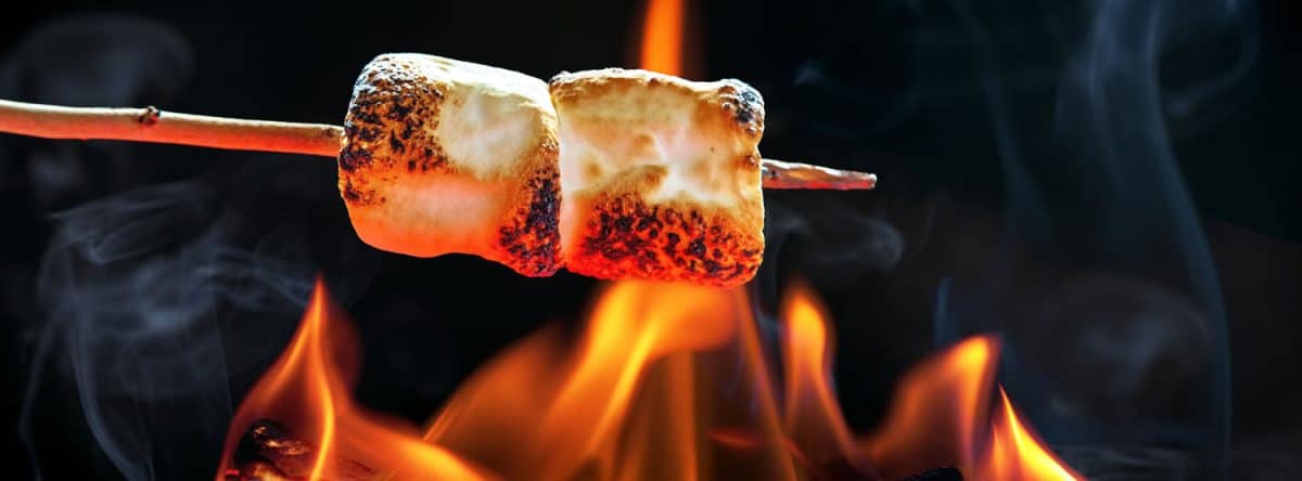 Two marshmallows roasting over fire flames
