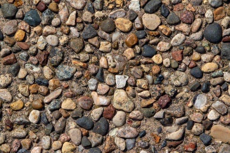 A vintage exposed aggregate stone patio surface in bright natural sunlight, Can You Resurface Exposed Aggregate [And How!]
