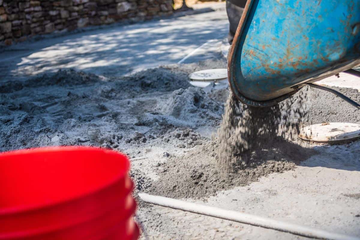 A wheelbarrow dumping polymeric paver sand onto an area where a new patio is being built, Does Polymeric Sand Come In Different Colors? [And Will It Darken Over Time?]