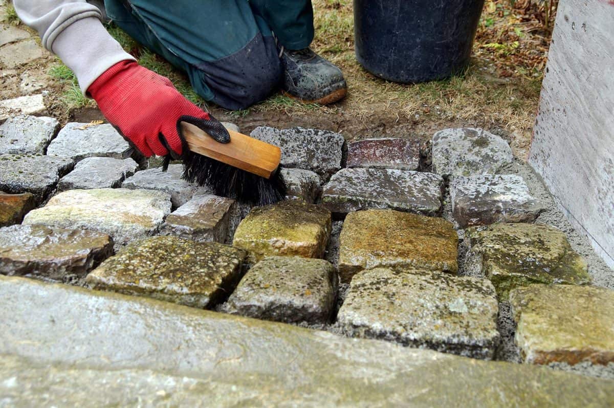 Worker cleaning concrete paver blocks with brush and water after laying paving stones