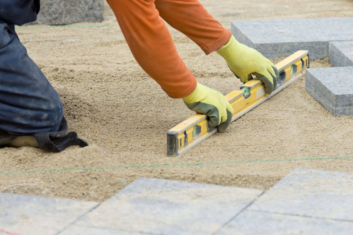 Worker using a level bara to even out the paver sand