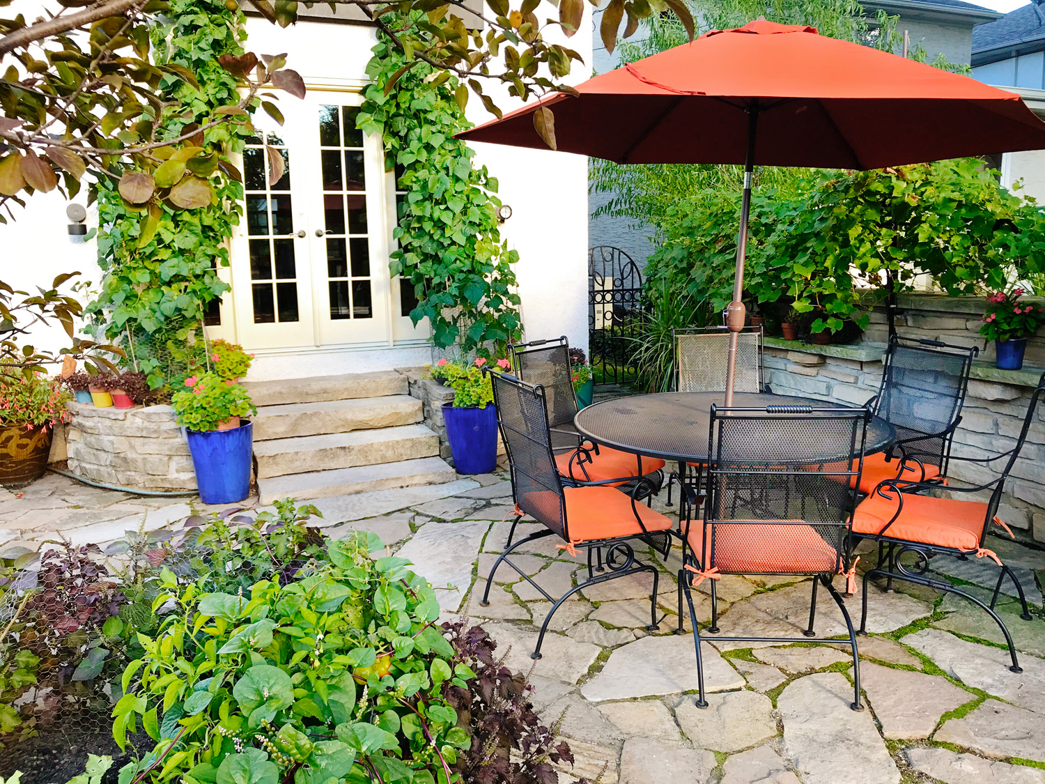 A residential home exterior. Backyard outdoor space with garden and patio and outdoor furniture and sun umbrella