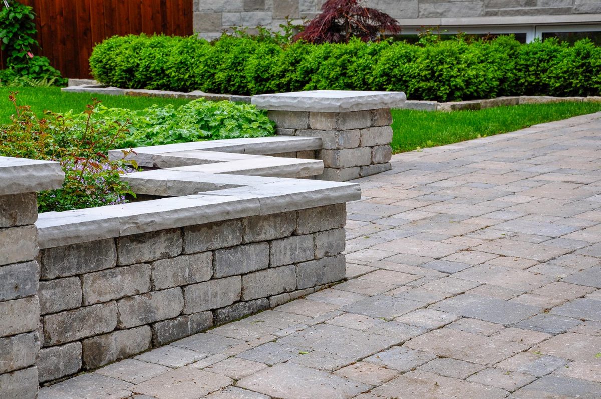 A seat wall with pillars and natural stone coping helps define a tumbled paver driveway and is a beautiful landscaping