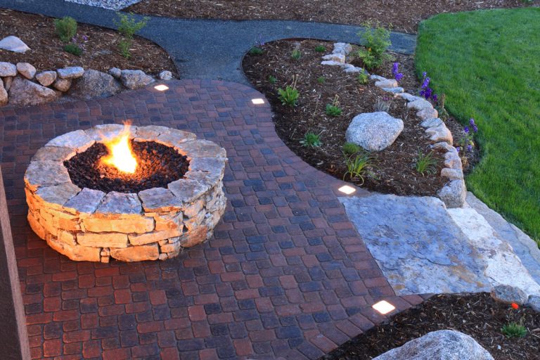 Aerial shot of fire pit and landscape pavers at dusk. Paver patio has built in lighted pavers, Best Patio Pavers For Cold Climates