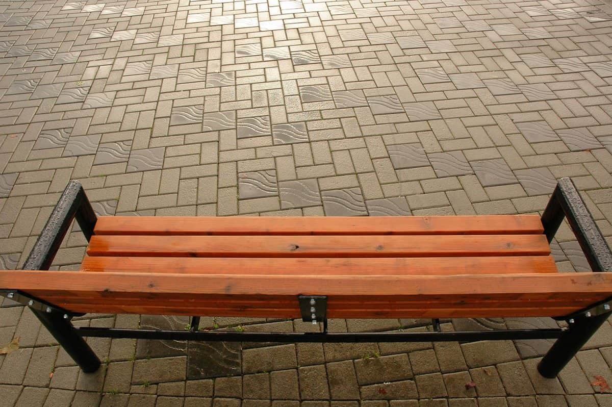 An overhead view of a park bench on a brick walkway