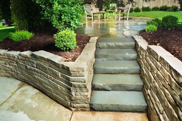 A beautiful landscaped back yard with outdoor patio furniture and ornamental gardens, Can You Use Pavers To Build A Retaining Wall?
