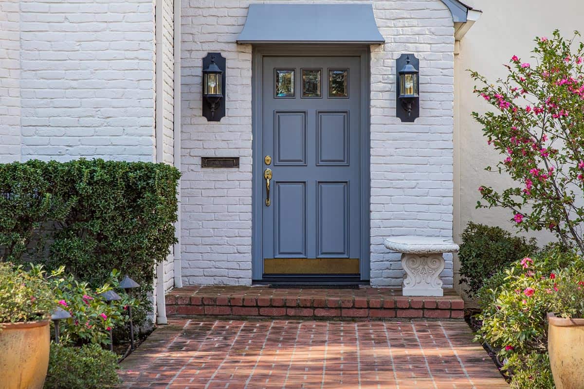Blue front door of traditional style home with brick entry and white brick exterior