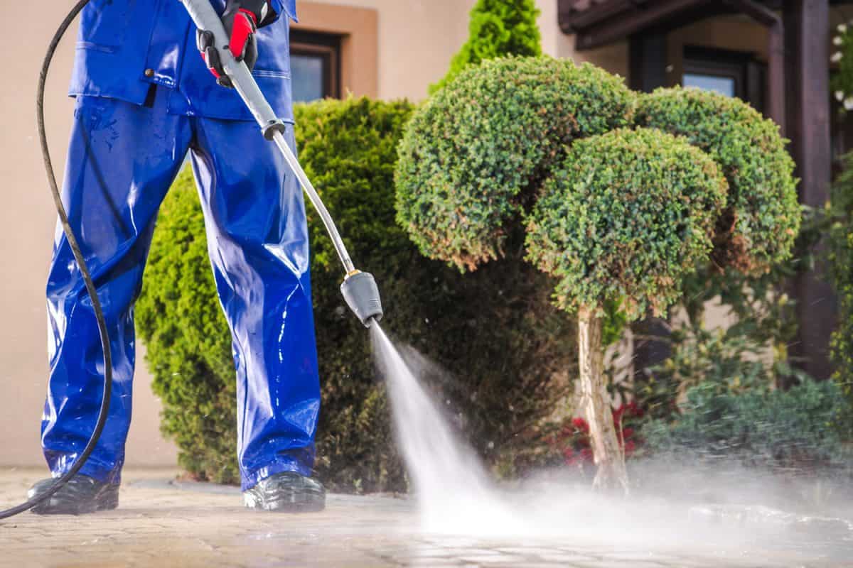 Caucasian Worker in His 30s with Pressure Washer Cleaning Residential Driveway. 