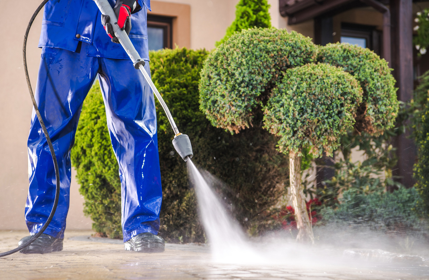 Caucasian Worker in His 30s with Pressure Washer Cleaning Residential Driveway. Garden and Home Surrounding Maintenance.