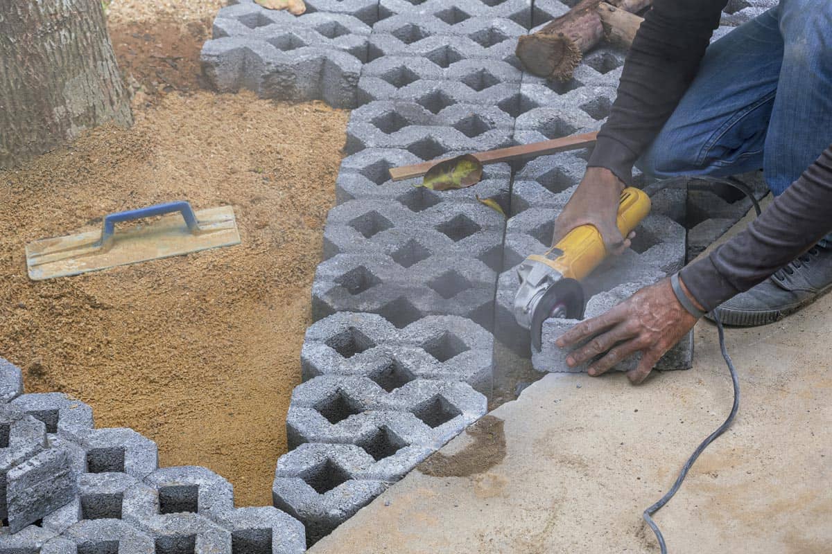 Construction worker's hand using electric grinder cutting turf stone block for paving sidewalk in public park area