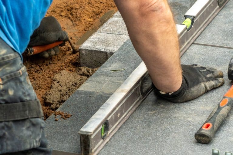 Expert workman laying patio edging bricks in garden makeover - Can You Lay Porcelain Pavers On Sand [And How To Install]