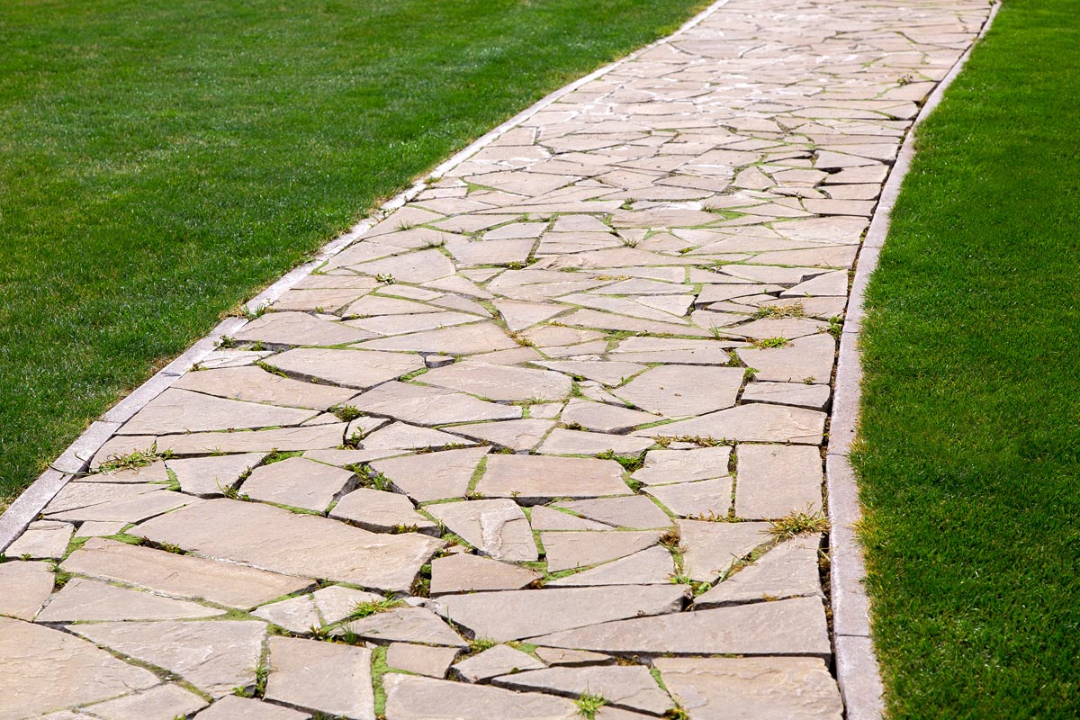 A flagstone footpath in a park with a green lawn, How Thick Should Flagstone Be For Walkway? For Patio?
