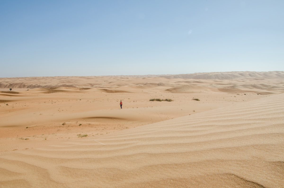 Girl walking alone through Wahiba sands deserts towards horizon
