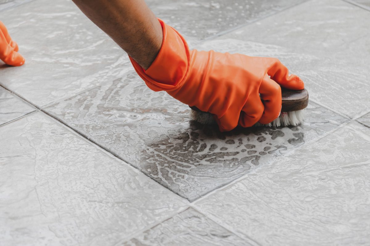 Hand of man wearing orange rubber gloves- is used to convert scrub cleaning on the tile floor.