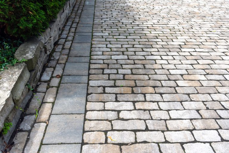 Hardscape precast concrete cobblestones are laid with a modern banding in the luxury landscaping driveway installation, 5 Types of Edging For Pavers