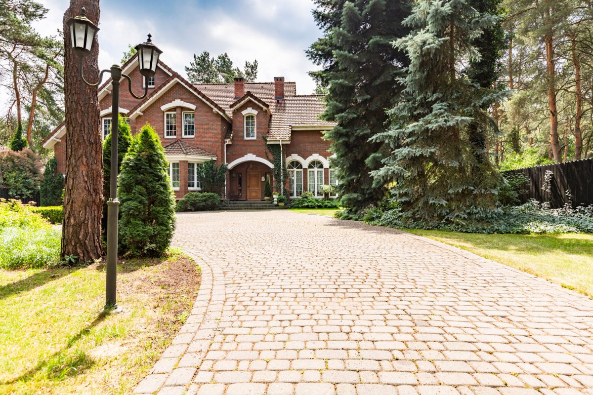 Luxurious private real-estate with a huge brick mansion with white trims and a brick pavers driveway