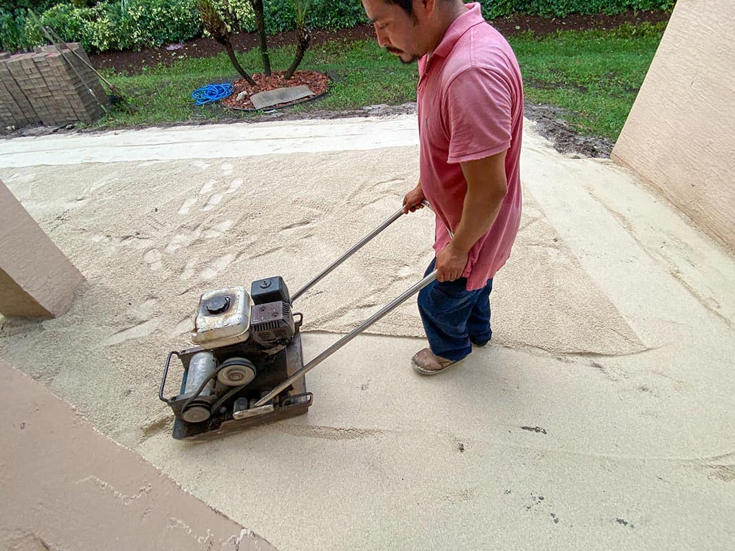 Male worker is using a compaction force plate compactor to prepare area for pavers