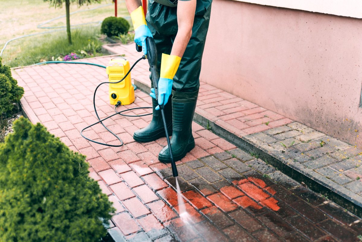 Man cleaning red, conrete pavement block using high pressure water cleaner. 