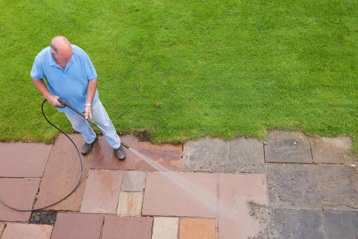 Man in his 60s washing his patio slabs with a pressure washer
