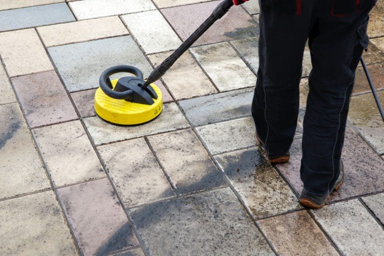 Man using a power sprayer to clean pavers, Can You Pressure Wash Pavers? [And How to Without Damaging Them]