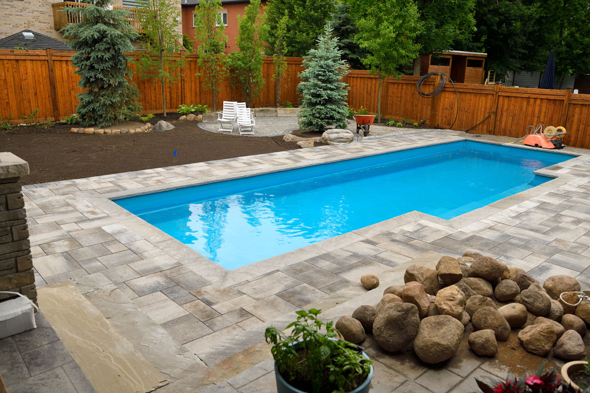 Newly installed swimming pool in Spring with unfinished, back yard landscaping construction ongoing, Types Of Pavers For Pool Deck