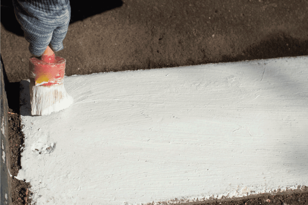 Paints the kerb with white paint. Brush with paint for the road curb