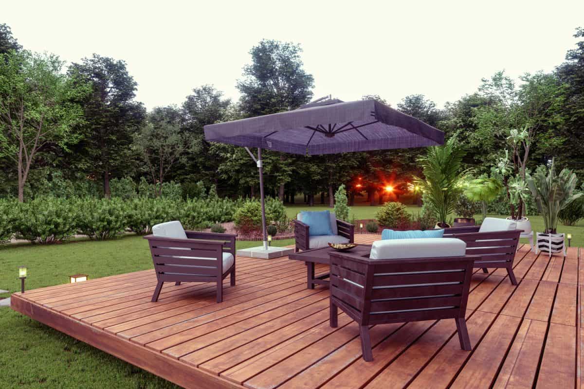Patio With Wooden Seats, Coffee Table And Sunshade In The Garden with Sunset View Background.

