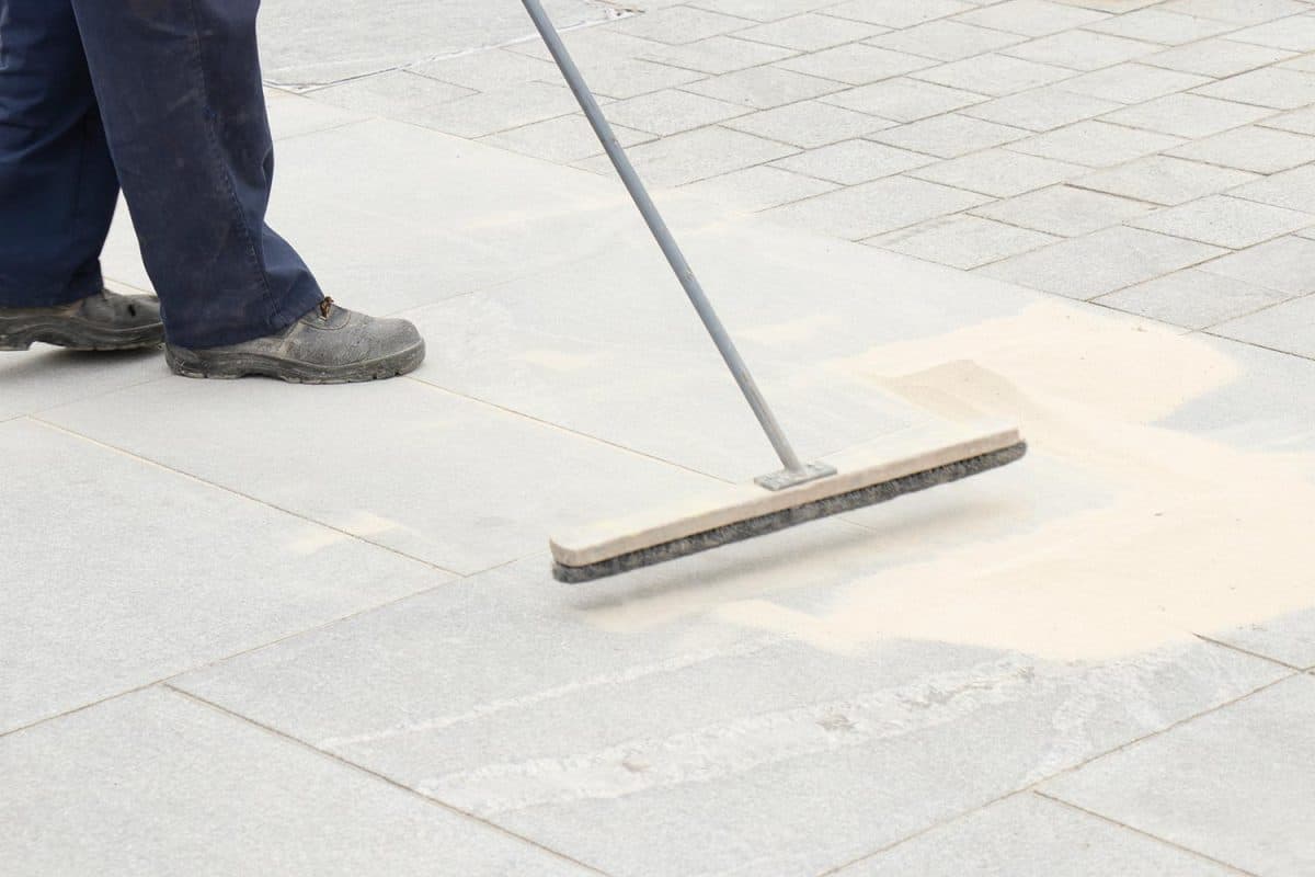 Pavement construction worker filling the block joints with sand using long broom