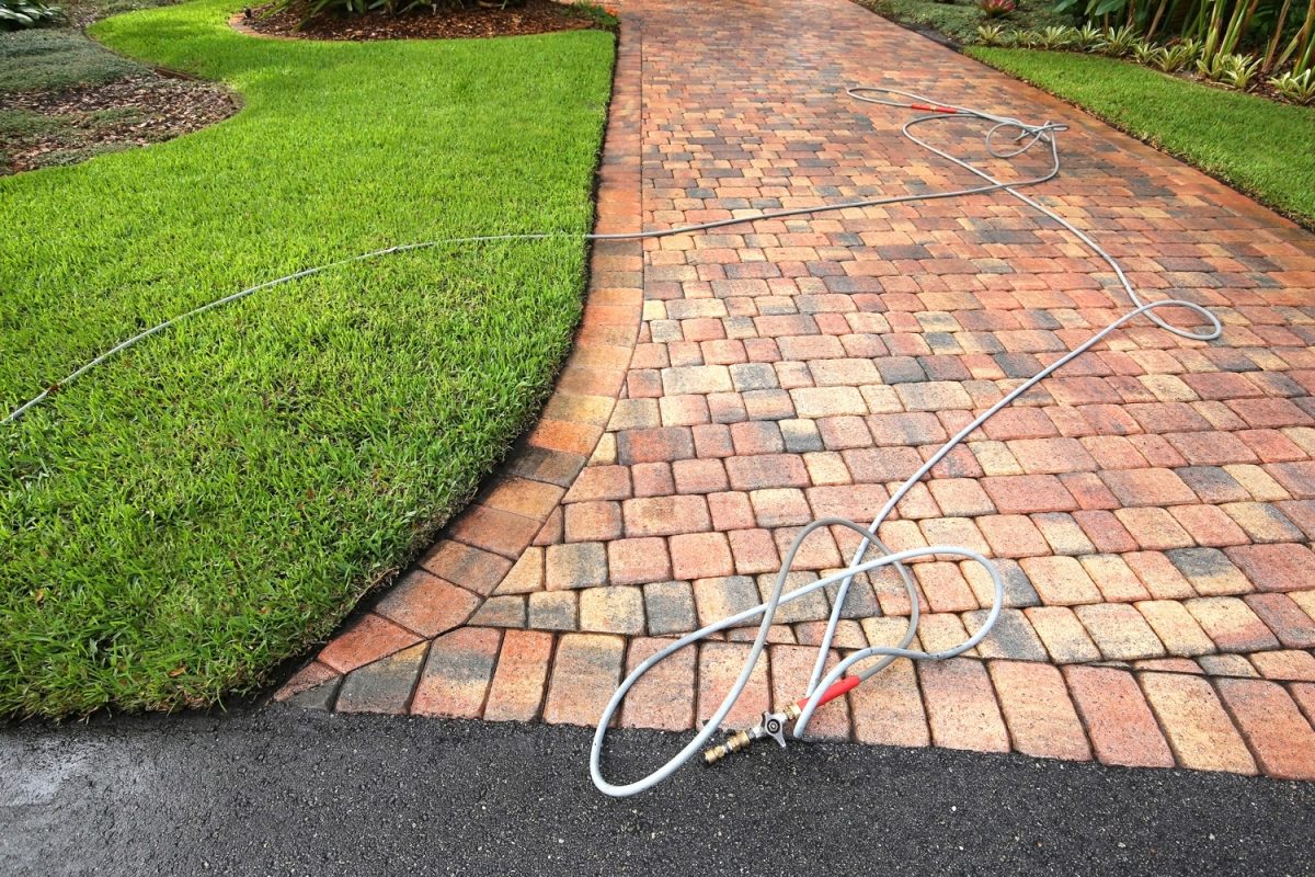 Paver driveway professionally pressure cleaned, with the hose and wand on the driveway.

