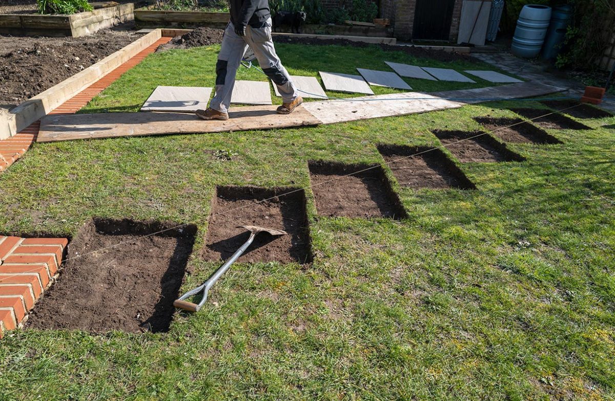 Rectangular sections cut into a lawn in preparation for concrete base and then stone stripping stone pathway installation