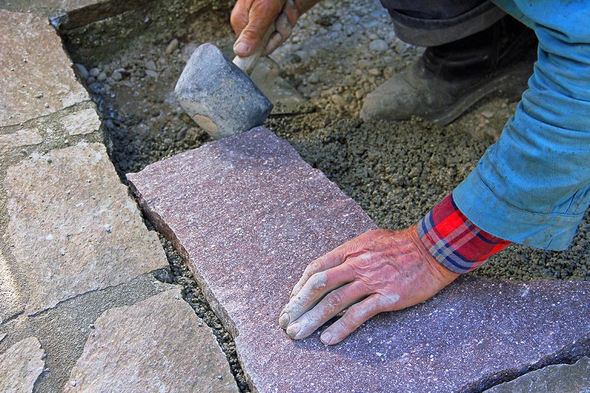Senior landscape gardener fitting a flagstone tile with a rubber mallet
