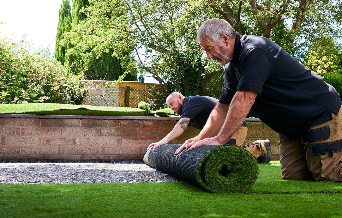 Two workers Installing artificial grass in modern garden of home