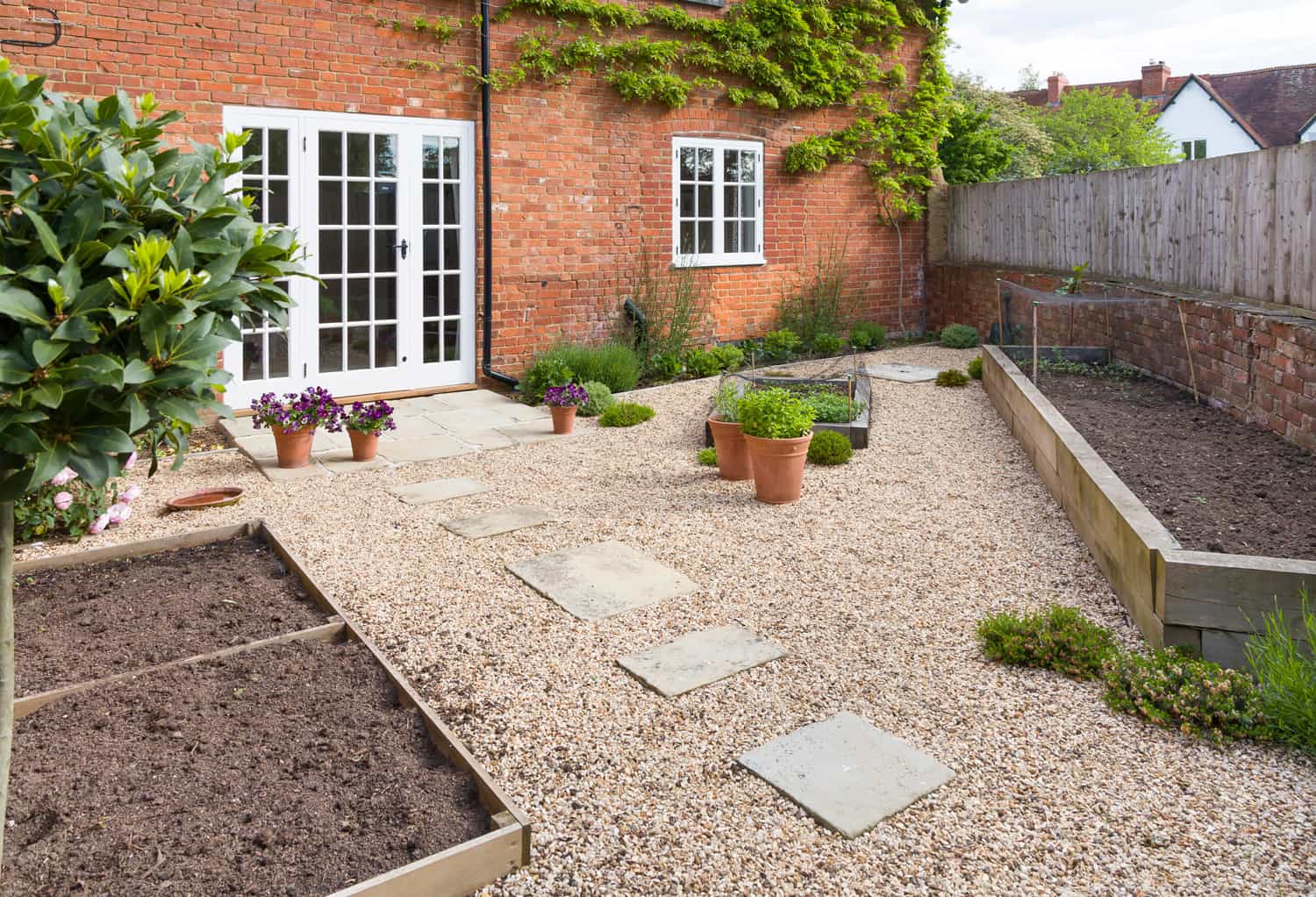 UK garden in spring with empty vegetable beds. Courtyard style Victorian garden with gravel and York stone paving.