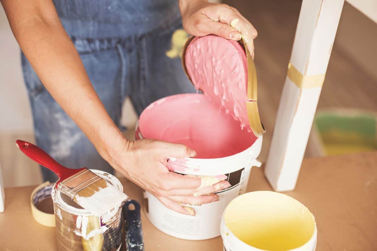 Woman is opening a paint can with pink paint.

