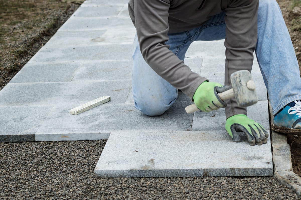 A worker hammering the stone plates to install in the walkway, How Thick Are Bluestone Pavers? [What Sizes Do Bluestone Come In?]
