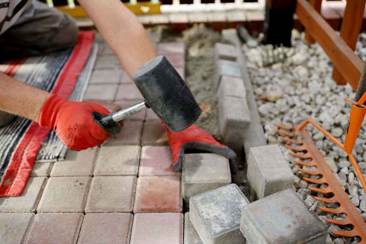 Worker holding a rubber mallet in installing a brick stone paver