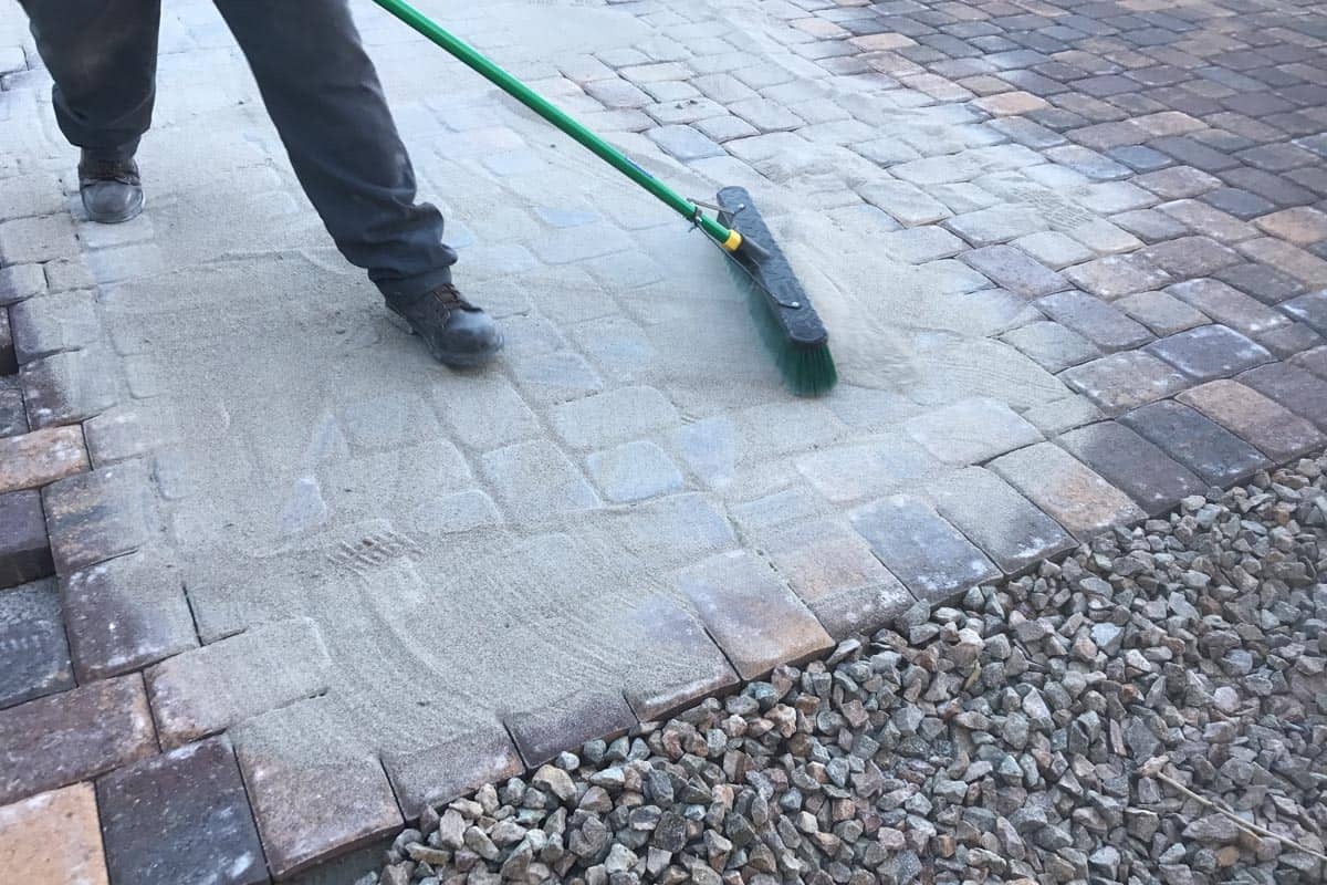 Worker spreads polymeric sand to the pavers