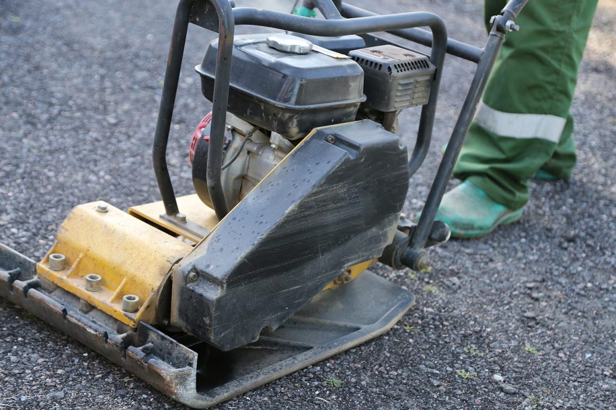 Worker uses vibratory plate compactor compacting asphalt