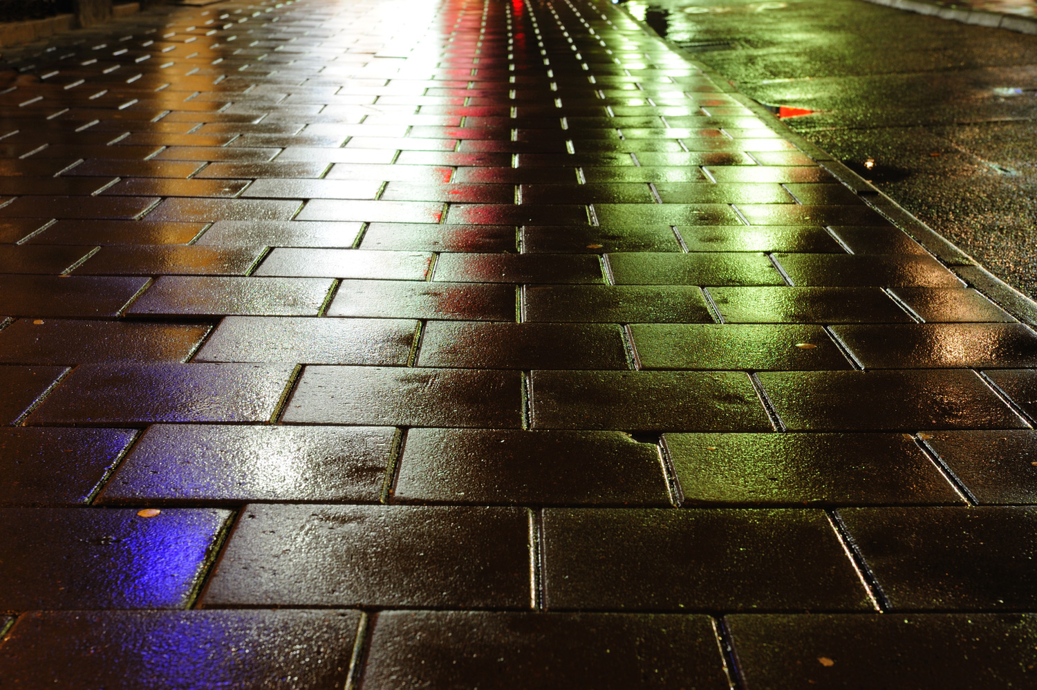 Rain wet sidewalk reflecting blue-white-yellow light