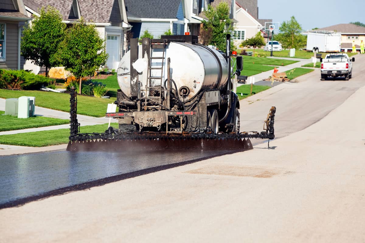 A spray truck is applying a black asphalt seal coat to a street
