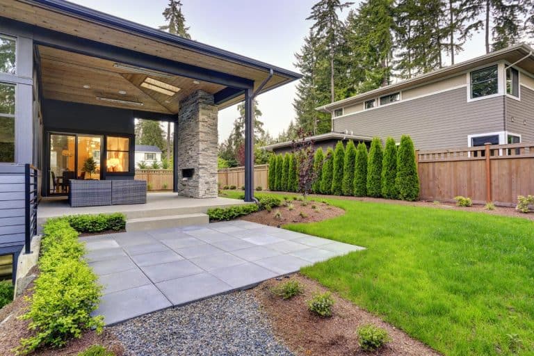 A new modern home features a backyard with covered patio accented with stone fireplace, Should Grass Be Level With Patio?