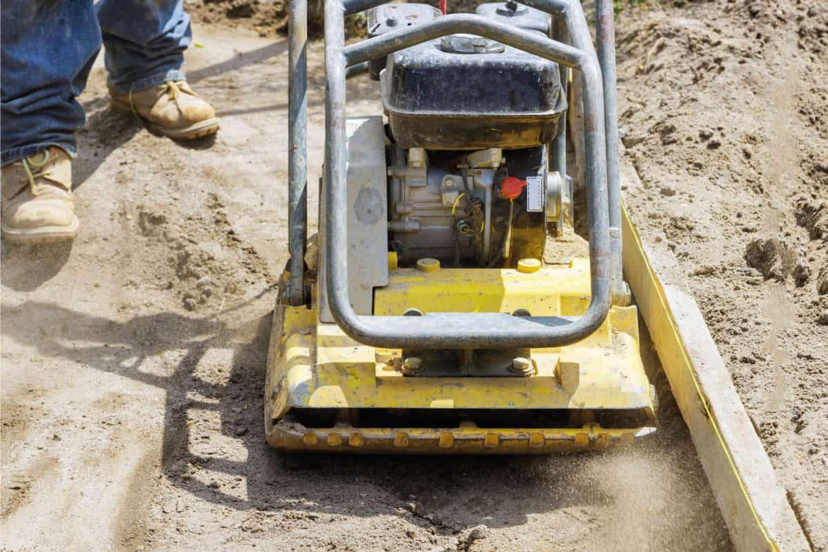 Vibratory plate compactor worker uses compactor to soil at worksite under construction