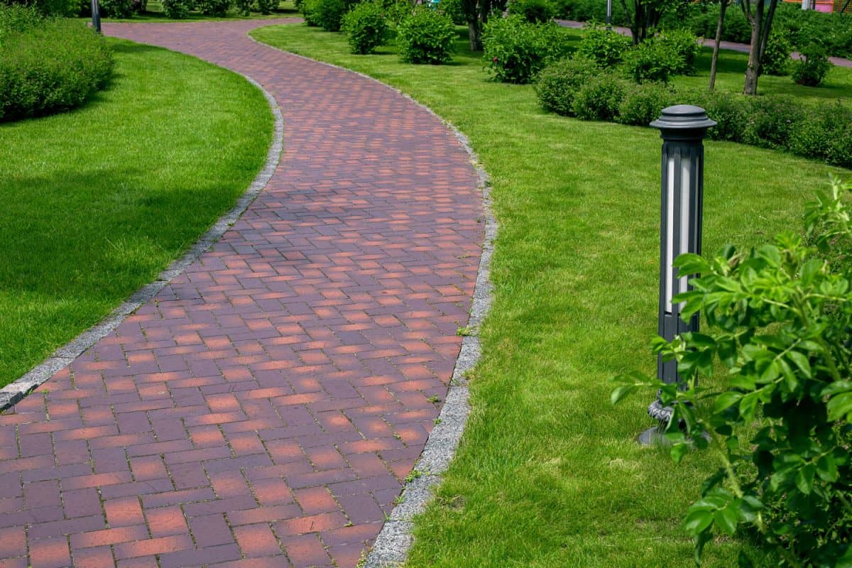 iron ground lantern garden lighting with curved path paved stone tiles in park among plants